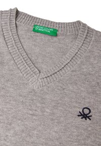 Šedý svetr s výstřihem do V a žebrovaným límcem. Obsahuje malé vyšívané logo v námořnické modři. Vyrobeno z měkké, texturované pleteniny.