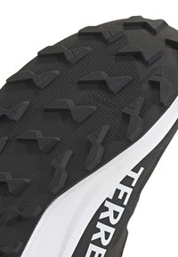 Μαύρη ελαστική σόλα παπουτσιού με σχεδιαστικό πέλμα που διαθέτει γωνιώδεις προεξοχές, πλαισιωμένη από λευκή πλευρική λεπτομέρεια με την επιγραφή "TERR".