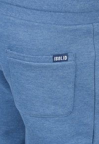Blue cotton sweatpants featuring a ribbed waistband and a single back pocket with a black and white "ISOLID" label. Smooth texture.
