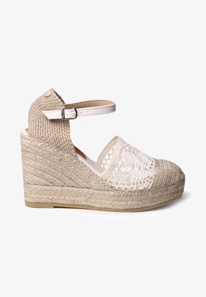 Sandale à talon compensé en tissu beige tissé avec un talon texturé, des détails en dentelle sur le devant et une sangle blanche à la cheville avec une boucle.