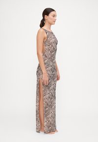 Abito lungo senza maniche con stampa zebra beige e marrone. Presenta spacchi laterali e una silhouette aderente. Realizzato in tessuto leggero e morbido.