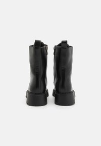 Botine negre din piele cu o finisaj neted, vârf rotund și o talpă groasă, texturată. Prezintă un fermoar în spate și un tab pentru a fi tras.