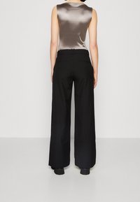 Bez rękawów, szara satynowa bluzka w połączeniu z czarnymi spodniami o szerokich nogawkach i wysokim stanem. Spodnie mają gładkie wykończenie i tylne kieszenie.