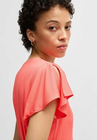 Coral-colored blouse with short flutter sleeves, featuring a smooth, lightweight texture and a subtle open shoulder design.