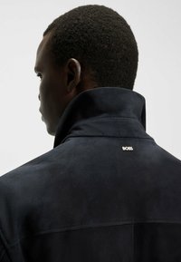 Navy suède jack met een hoge kraag en subtiele "BOSS" logo op de achterkant. Soepele textuur met een nette stikselverwerking.