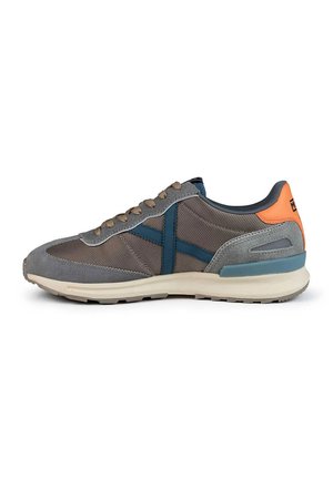Zapatilla deportiva gris con materiales de malla y gamuza. Presenta acentos en azul, cordones beige y una lengüeta trasera naranja. Suela lisa para tracción.