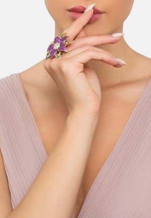 Purple flower-shaped ring with gold accents; center adorned with a clear stone; worn on a finger, displaying a smooth, elegant design.