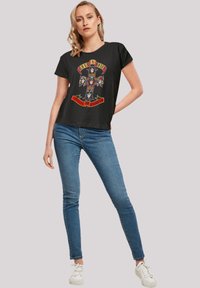 Black short-sleeve t-shirt featuring a colorful graphic with skulls and a cross, text includes "Guns N' Roses" and "Appetite for Destruction."
