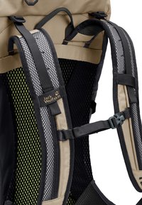 Gros plan sur les bretelles beige et noires d'un sac à dos Jack Wolfskin avec un rembourrage en maille et une boucle de poitrine réglable.