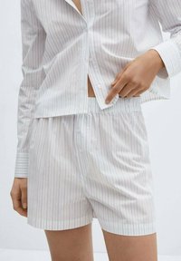 Vitt bomullspyjamas-set bestående av vertikala blå ränder, inklusive en skjorta med knappar och shorts med elastisk midja och slät textur.