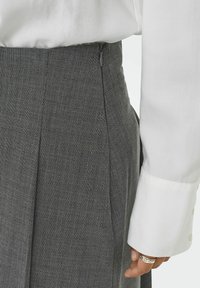 Falda gris con diseño a rayas finas y cuadros, con cremallera lateral y pliegues. Combinada con una camisa blanca de manga larga. Tejido texturizado.