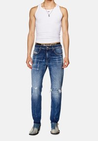 Slim-fit blå denimjeans med slitna detaljer, blekta partier, femficksdesign och ett mörkt midjeband. Bärs med en vit linne och stövlar.