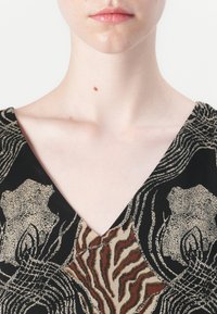 Blusa a scollo a V con stampa animale nei colori nero, beige e marrone. Presenta una texture di tessuto liscia e motivi astratti che ricordano la pelliccia e le strisce.