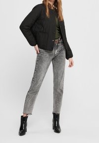 Sort quiltet jakke med trykknapper, grøn skjorte, falmede grå jeans og sorte hælankelstøvler. Simpelt design med tekstureret stof.