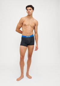 Boxers noirs avec une ceinture logo Levi's bleue, conçus pour le confort. Tissu lisse et forme ajustée, portés par un modèle masculin debout.