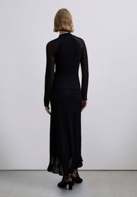 Top negro de manga larga con textura acanalada y cuello alto simulado, combinado con una falda larga a juego que presenta un dobladillo con flecos y una textura ligera.