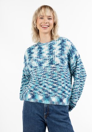 Strickpullover in Blau- und Weißtönen mit einem strukturierten Muster. Besitzt einen runden Ausschnitt und überschnittene Schultern, kombiniert mit hoch taillierten Jeans.