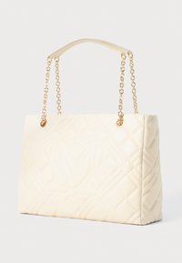 Κρεμί σοφιστικέ τσάντα με καπιτονέ σχέδιο, χρυσές αλυσίδες και ραμμένο λογότυπο στην μπροστινή πλευρά, ορθογώνια μορφή, τοποθετημένη σε λευκό φόντο.
