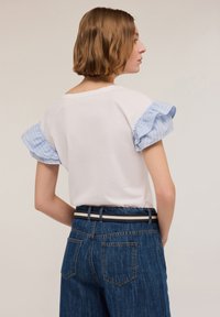 T-shirt bianca con maniche a ruffles a strisce azzurre, abbinata a jeans blu scuro a vita alta con una cintura a strisce in contrasto.