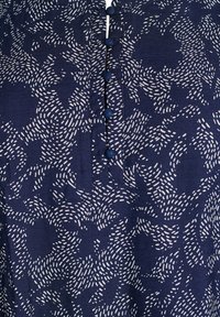 Chemise bleu marine ornée d'un motif floral avec des accents blancs, cinq boutons bleus sur le devant, et un tissu doux et texturé.