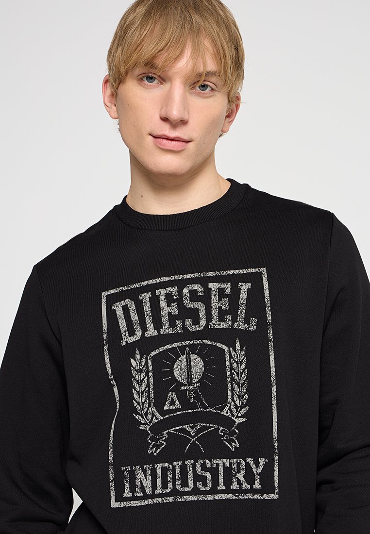 Felpa nera con stampa grafica testurizzata della parola "DIESEL" e un emblema con una mano che tiene una spada, su uno sfondo leggermente rigato.
