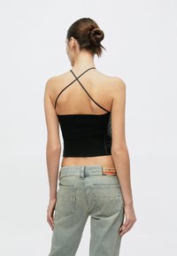 Μαύρο κοντό τοπ με ριγέ υφή και λουριά σε σχήμα σταυρού, συνδυασμένο με ανοιχτόχρωμο τζιν παντελόνι που διαθέτει λογότυπο και κλασικό σχέδιο πίσω τσέπης.