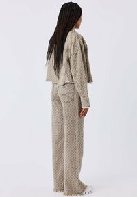 Conjunto de dos piezas hecho de tela beige texturizada. La chaqueta corta presenta bordes deshilachados. Los pantalones de pierna ancha tienen un patrón a juego y dobladillos deshilachados.