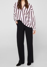 Camicia a maniche lunghe bianca con strisce rosse e blu navy, design a scollo a v, abbinata a pantaloni neri a vita alta e scarpe nere.