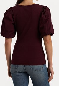 Burgunderröd topp med puffärmar. Mjukt, stretchigt tyg med en figurnära silhuett. Slät textur och rund halslinning. Matchad med blå jeans.