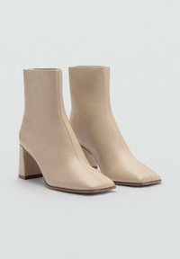 Beige læder ankelstøvler med firkantet tå, der har et afdæmpet design og en blokhællængde midt på. Synlige syninger som detajler.