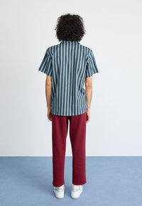 Short-sleeve, striped shirt in blue and green, paired with burgundy pants. Features a straight cut and relaxed fit. White sneakers complete the outfit.