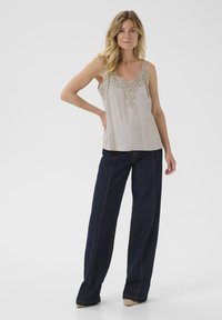 Svetlo bež brezrokavnik s čipkastim detajlom na izrezu, v kombinaciji s temno jeans širokimi hlačami z kontrastnim šivanjem in sproščenim krojem.