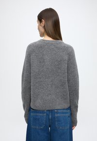 Szürke kötött pulóver kerek nyakkivágással, laza szabással és hosszú ujjakkal, puha anyagból. Kék farmer széles szárú nadrággal párosítva.