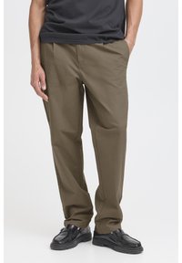 Khaki pants with a relaxed fit, flat front, and side pockets. Paired with black shoes, the fabric has a smooth texture and neutral tone.