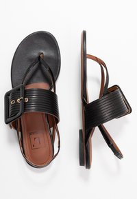 Sandali neri con una ampia fascia rigata, grande fibbia nera, soletta in pelle liscia e sottopiede marrone discreto; design con suola piatta.