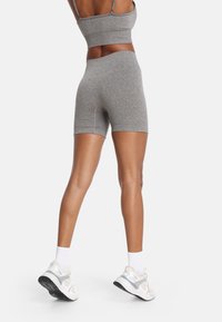 Sivý športový crop top a zodpovedajúce šortky, vyrobené z textúrovaného materiálu, s priliehavým strihom a minimálnymi švami. Nosí sa s bielymi ponožkami a teniskami.