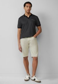 Polo grigio scuro con scollatura a V, maniche corte e taschino sul petto; abbinato a pantaloni corti beige chiaro e sneaker bianche con dettagli neri.