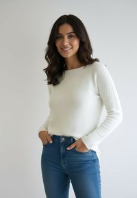 Biały sweter z dzianiny z długimi rękawami, luźnym krojem i miękką teksturą, zestawiony z niebieskimi, wysokim stanem jeansami. Prosty, czysty design.