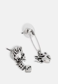 Silver earrings featuring a skull with flames and dice, secured with a metal pin, showcasing a shiny, reflective texture and intricate details.