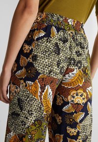 Pantalon à taille élastique avec un motif floral coloré, comprenant des tons de bleu marine, vert, orange et blanc, confectionné dans un tissu léger.