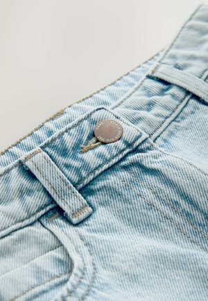 Vaaleansiniset farkut, joissa nappikiinnitys, kontrastitikkaukset, vyölenkki ja teksturoitu kangaskuvio.