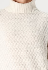 Πλεκτό πουλόβερ με ψηλό γιακά σε κρέμα, που διαθέτει υφασμάτινο σχέδιο κυψέλης, ριγωτό γιακά και μαλακό υλικό για άνεση.