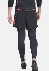 Pantaloni sportivi neri con accenti rossi, abbinati a leggings neri. L'outfit presenta un tessuto traspirante e elasticizzato con un design aderente.