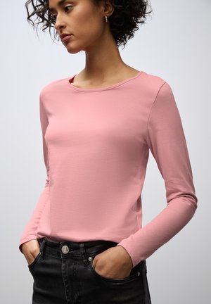Langärmliges, pinkes Oberteil aus weichem Material, mit rundem Ausschnitt und tailliertem Schnitt, kombiniert mit dunklen Jeans. Keine sichtbaren Muster.