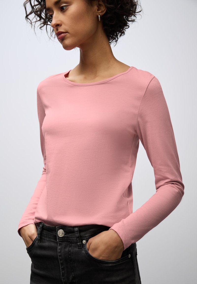 Pink long-sleeve top made from soft material, featuring a round neckline and a fitted silhouette, paired with dark jeans. No visible patterns.