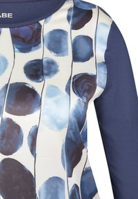 Kurzarmoberteil mit einem blauen und weißen abstrakten Punktmuster und einem marineblauen strukturierten Ärmel. Glattes Material und runder Halsausschnitt.