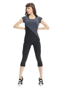 Maglietta atletica aderente in grigio e nero con maniche corte e design a blocchi di colore diagonali, abbinata a leggings neri a capri e sneakers nere.