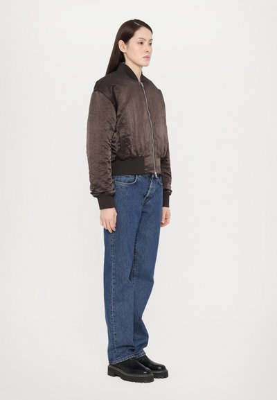 Brun bomberjakke med satinfinish, glidelås og ribbestrikkede mansjetter, kombinert med avslappede blå jeans og kraftige svarte støvler.