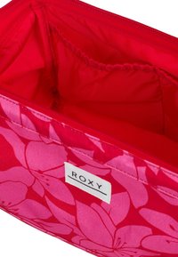 Roxy pink cosmetic bag featuring a floral pattern, smooth fabric, zip closure, and a lined interior with an elastic pocket.