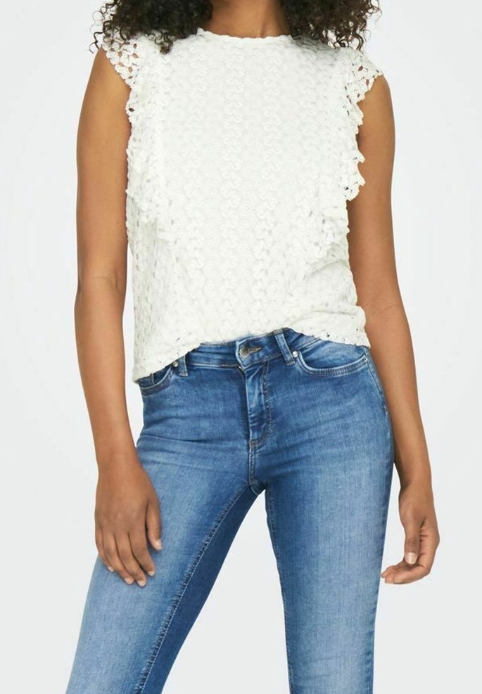 Weiße Rüschenbluse aus strukturiertem Stoff mit Spitzenärmeln. Kombiniert mit enganliegenden blauen Denim-Jeans. Insgesamt ein lässiger, geschichteter Look.